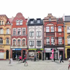 Kolorowe kamienice na lęborkim starym mieście, z witrynami sklepów i przechodniami na brukowanym placu.