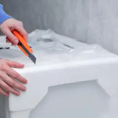 Ręce tnące pomarańczowym nożem styropianowe opakowanie telewizora.