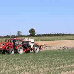 Czerwony traktor z opryskiwaczem na polu. Prawidłowa kolejność mieszania środków ochrony roślin zapewnia skuteczne działanie.