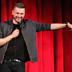 Mateusz Socha na scenie z mikrofonem, na tle czerwonej kurtyny.