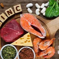 Zink-reiche Lebensmittel wie Rindfleisch, Lachs, Garnelen, Kürbiskerne, Käse, Spinat, Mandeln, Pilze und Knoblauch sind auf einem Holztisch arrangiert.