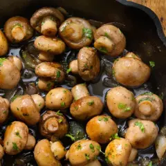 Champiñones al ajillo recién hechos en sartén de hierro fundido, con perejil picado y un toque de ajo.