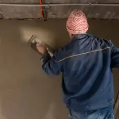 Mann mit Mütze verputzt eine Wand im Keller. Der **Sanierputz** im **Keller** wird sorgfältig aufgetragen.
