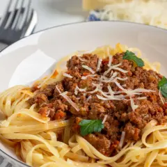 Teller mit Spaghetti Bolognese, garniert mit Parmesan und Petersilie. Ja, man kann gekochte Spaghetti Bolognese einfrieren.
