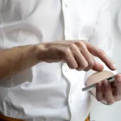 Mężczyzna w białej koszuli prowadzi rozmowę telefoniczną po angielsku, dotykając ekranu smartfona.