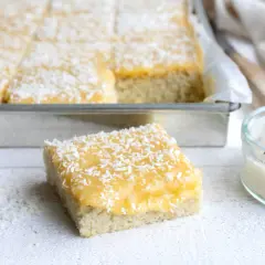 En bit av en saftig silviakaka i långpanna, toppad med gul glasyr och kokosflingor.