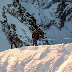 Dwóch alpinistów na śnieżnym grzbiecie, przygotowuje się do wspinaczki na Mera Peak. Słońce oświetla zbocza.