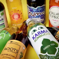 Flera flaskor kombucha, en dryck som många anser vara nyttig, ligger utspridda. Olika märken som Captain Kombucha, Karma Kombucha och Hallands Kombucha syns tydligt.