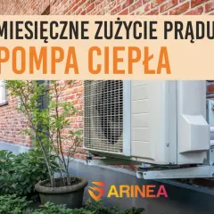 Pompa ciepła zamontowana na ścianie z cegły. Napis informuje o miesięcznym zużyciu prądu przez pompę ciepła.