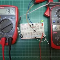 Układ na płytce stykowej z diodami LED, rezystorem i dwoma multimetrami. Jeden mierzy napięcie 13.7V, drugi prąd 05.16A.