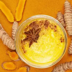 Goldene Milch mit Kurkuma und Honig, verziert mit Sternanis. Umgeben von frischen Kurkumawurzeln und Pulver.