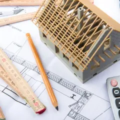 Model domu, miarki, ołówek i kalkulator na planach budowlanych. To narzędzia do stworzenia kosztorysu do kredytu hipotecznego.