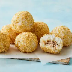 A delicious tuna bento box features rice balls coated in sesame seeds, with one cut open to reveal the tuna filling.