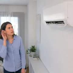 Mujer escucha atentamente el **ruido del aire acondicionado**, preocupada por un sonido inusual.