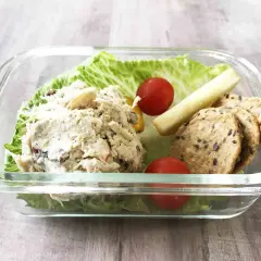A delicious chicken salad bento box with lettuce, cherry tomatoes, a pickle spear, and crackers.