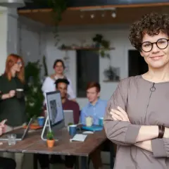 Kobieta w okularach, pewna siebie, osoba która lubi być w centrum uwagi, stoi przed zespołem w biurze.