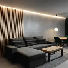 Nowoczesny **styl industrialny salon loft** z szarą sofą, drewnianą ścianą i zielonymi akcentami.