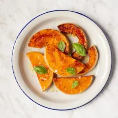 Rodajas de calabaza al horno, glaseadas y con hojas de albahaca fresca, servidas en un plato blanco con borde azul.