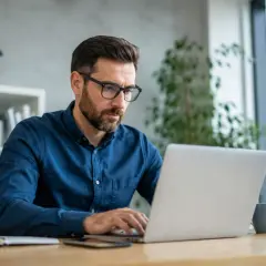 Mężczyzna w okularach pracuje przy laptopie, planując zmianę nazwy firmy w CEIDG.