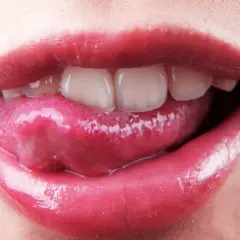 Labbra lucide e lingua che esce, mostrando i denti. La saliva è disinfettante, un piccolo segreto di bellezza naturale.