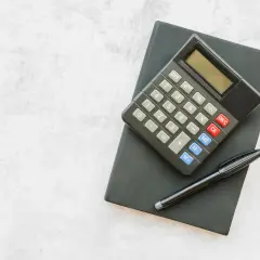 Kalkulator i długopis na czarnym notesie. Obliczanie, ile urlopu na pół etatu, to proste zadanie.