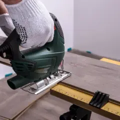 Mit einem Stichsäge wird Laminat schneiden. Ein Handwerker mit Handschuhen arbeitet präzise.