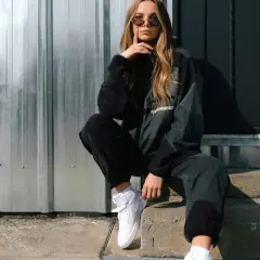 Chica con estilos de ropa mujer modernos, posa con sudadera y pantalones deportivos, zapatillas blancas y gafas de sol.