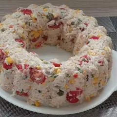 Salade de riz en forme de couronne, garnie de tomates cerises, maïs et persil.