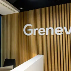 Nowoczesne biuro z logo Grenevia na drewnianej ścianie. Za oknem błękitny, deszczowy krajobraz miejski.