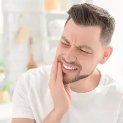 Uomo con mano sulla guancia, espressione di dolore ai denti, forse un problema al solco gengivale.