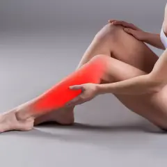 Kobieta masuje łydkę, gdzie czerwony obszar wskazuje na ból mięśnia płaszczkowatego.