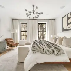 A luxurious bedroom with modern decor, featuring a plush fur throw on the bed, abstract art, and a statement chandelier.