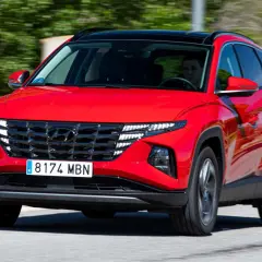 Un conductor prueba el Hyundai Tucson híbrido enchufable rojo, con su distintiva parrilla y luces LED, circulando por una carretera.