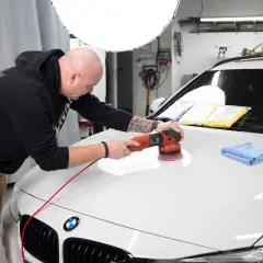 Man polerar en vit bil med maskin för att få en perfekt finish.