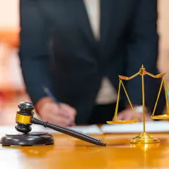 Młotek sędziowski i waga sprawiedliwości na biurku. Prawnik pisze dokument, który może dotyczyć podziału majątku i właściwości sądu.