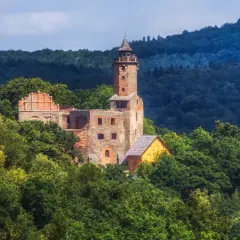 Ruiny zamku na wzgórzu otoczone lasem, w oddali widać jezioro Bystrzyckie.