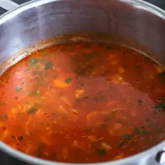 Gorąca zupa pomidorowa w garnku, z widocznymi kawałkami warzyw i zieleniną. Czy zupę pomidorową zaprawia się mąką?