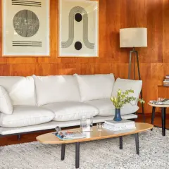 A modern living room with a white sofa, art, and a floor lamp, all set against warm wood tones.
