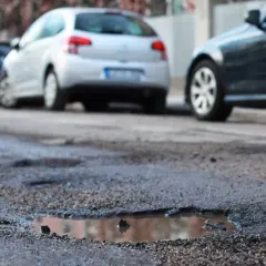 Poprzeczna nierówność jezdni z kałużami i zaparkowanymi samochodami.
