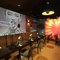 Szukasz miejsca, gdzie zjeść w Szczecinie? Wnętrze restauracji z azjatyckim klimatem, wielkoformatowym zdjęciem kobiety jedzącej pałeczkami i grafiką wschodzącego słońca.