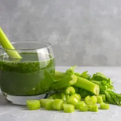 Szklanka orzeźwiającego soku z selera, z łodygą w środku, obok świeżych, pokrojonych kawałków selera.