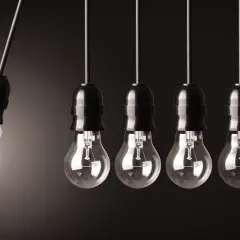 Wisząca żarówka energooszczędna, świecąca, obok rzędu tradycyjnych żarówek. Symbolizuje zmianę, innowację i oszczędność jednostki napięcia.