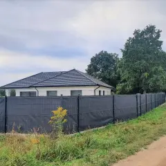 Nowoczesna siatka ogrodzeniowa skutecznie zasłania płot, zapewniając prywatność. Dom i samochód w tle.