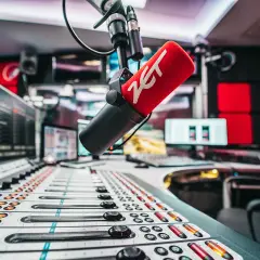 Mikrofon radiowy z logo ZET na tle konsolety i monitorów w studiu.