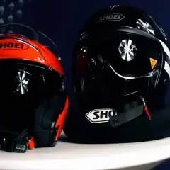 Dwa kaski motocyklowe Shoei: jeden czerwono-czarny, drugi czarny. Oba mają widoczne zapięcie kasku DD.