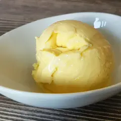 Cremiges Mango-Eis, selbst gemacht mit der Eismaschine, in einer weißen Schale auf Holztisch.