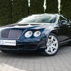 Elegancki, ciemnogranatowy Bentley Continental GT, brytyjski producent luksusowych aut, zaparkowany przed żywopłotem.