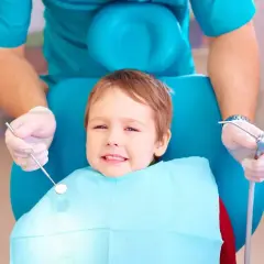 Mały pacjent u dentysty, który szuka odpowiedzi: co na ból zęba u dziecka. Dentysta w rękawiczkach trzyma narzędzia.