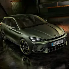 Nowoczesny, zielony Cupra kombi z ciemnymi felgami stoi na mokrej nawierzchni w industrialnym otoczeniu.