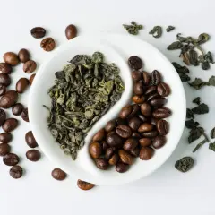 En vit skål delad i två, med grönt te och kaffebönor. En evig kamp mellan te eller kaffe.